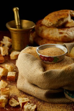 Özbek, ahşap bir masa üzerinde havan, çuval ve geleneksel yassı ekmekle kırsal bir yaşam kompozisyonu içinde kurutulmuş ekmek ve ekmek kırıntıları.