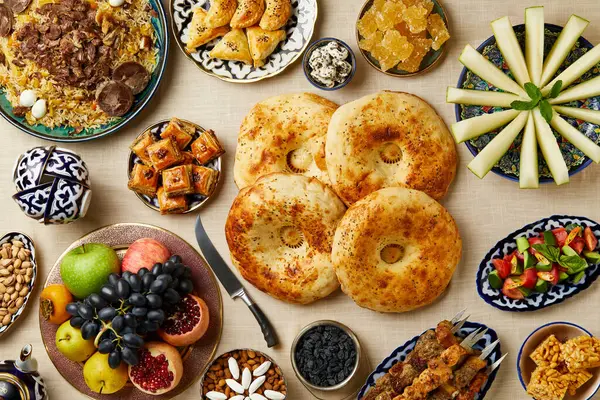 Geleneksel Özbek sofrasında pilav, yassı ekmek, meyve, tatlı ve kebap gibi çeşitli ulusal yemekler var. Üst görünüm.