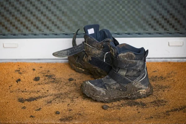 Muddy dirty children\'s shoes leaving mud on doorstep rug.