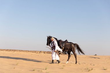 Saudi arabian man riding on his black stallion in a desert clipart
