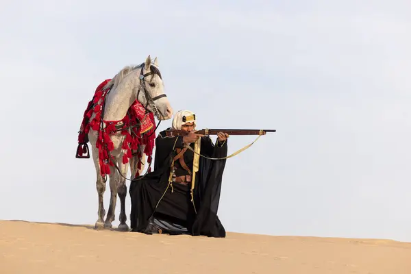 Saudi man hunting in the desert, aiming his rifle