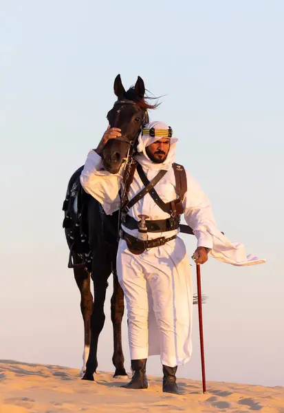 stock image Man in traditional Saudi Arabian clothing in a desert with a black stallion