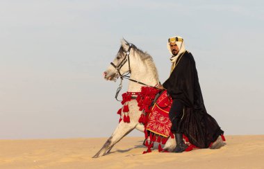 Beyaz aygırıyla geleneksel giyinmiş Suudi bir adam.