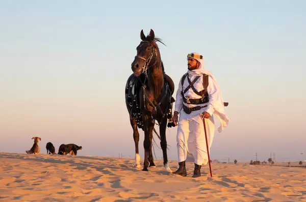 stock image Man in traditional Saudi Arabian clothing in a desert with a black stallion