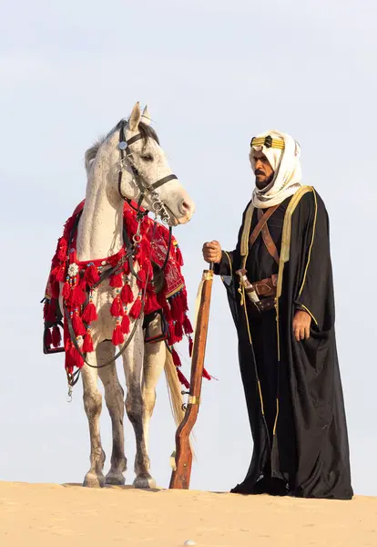 Saudi man in traditional clothing with his white stallion