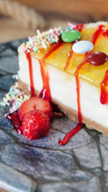 Tahta masanın üzerinde bir dilim limonlu cheesecake, üzeri şekerle kaplı ve yanında çilekle servis ediliyor.