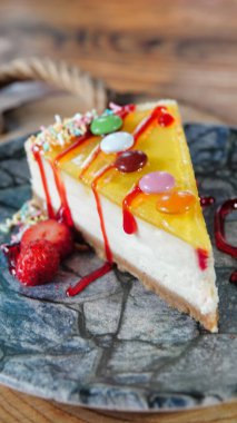 Tahta masanın üzerinde bir dilim limonlu cheesecake, üzeri şekerle kaplı ve yanında çilekle servis ediliyor.