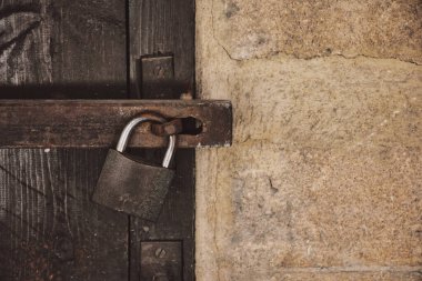 Close up view of a rusty padlock on weathered vintage wooden door with an old castle stone wall. Old Vintage Padlock Lock On Old Wooden Castle Door.