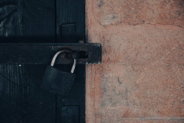 Close up view of a rusty padlock on weathered vintage wooden door with an old castle stone wall. Old Vintage Padlock Lock On Old Wooden Castle Door.