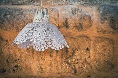 An old decorative lamp covered in lace, standing against a tumbled stone wall background with heart and light effects. Home decoration concept, vintage wallpaper, copy space.