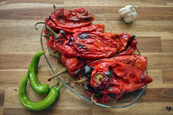 Roasted plump and bright red peppers in a clear glass dish with a head of garlic and green peppers on a wooden table. Healthy eating food low carb ketogenic diet