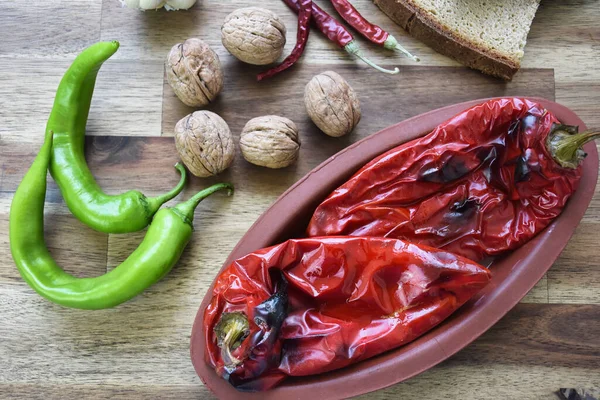 Roasted red peppers in a ceramic pot on a wooden table, accompanied by two slices of traditional natural wheat bread, red and green peppers, a head of garlic. Healthy eating food low carb diet