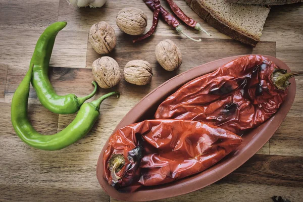Roasted red peppers in a ceramic pot on a wooden table, accompanied by two slices of traditional natural wheat bread, red and green peppers. Healthy eating food low carb diet