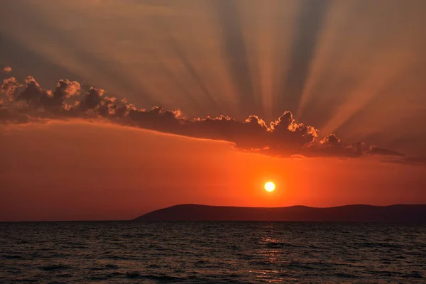 Beautiful Aegean sunset over Seferihisar hills in Izmir with an orange evening sky and light reflected in a dark calm sea
