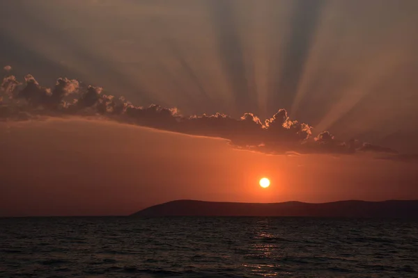 Beautiful Aegean sunset over Seferihisar hills in Izmir with an orange evening sky and light reflected in a dark calm sea