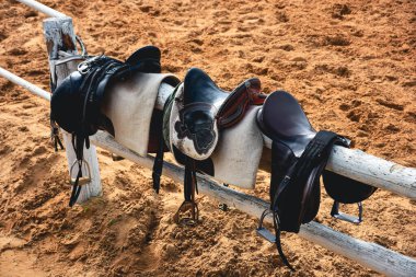 Horse saddles and bridles standing on fence at horse farm on training track 