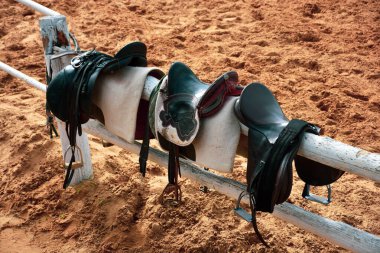 Horse saddles and bridles standing on fence at horse farm on training track  clipart