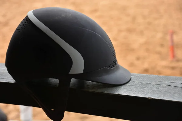 Close up view of  black Equestrian helmet with blurred horse farm view. Isolated Horse riding hat on the railing in the horse farm.