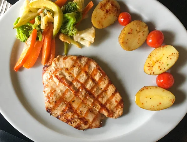 Terbiye edilmiş ızgara sağlıklı tavuk göğsü. Yaz barbeküsünde pişirilmiş. Tahta tahtada taze otlar ve limon suyuyla servis edilmiş.