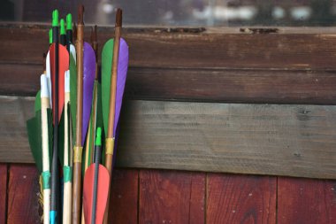Colorful traditional archery arrows leaning vertically on colorful wooden panel. Ethnic sport background