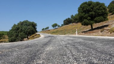 View of sky, trees, maquis, and clouds along a worn asphalt road in an Aegean town. Nature and sky landscape on a weathered asphalt mountain road. Gokceada Turkey