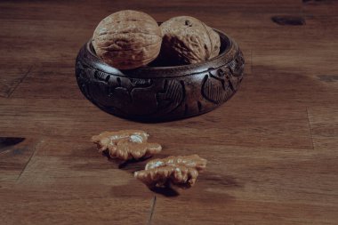 piles of walnuts waiting to be cracked in a wooden bowl on a wooden table. A walnut is cracked and its inside is visible. Organic healthy eating