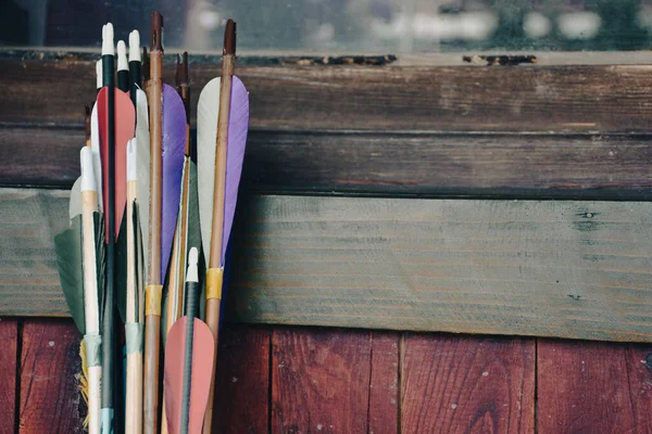 Colorful traditional archery arrows leaning vertically on colorful wooden panel. Ethnic sport background