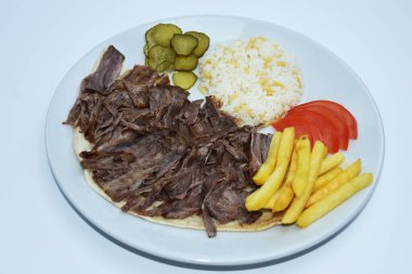Top view of Iskender doner kebab with rice, fried potatoes, tomatoes and pickled cucumbers served on a white plate