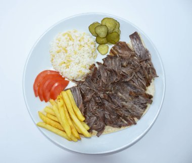 Top view of Iskender doner kebab with rice, fried potatoes, tomatoes and pickled cucumbers served on a white plate