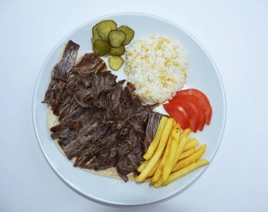 Top view of Iskender doner kebab with rice, fried potatoes, tomatoes and pickled cucumbers served on a white plate