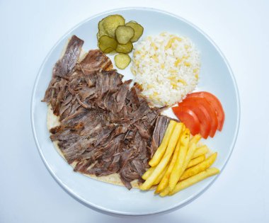 Top view of Iskender doner kebab with rice, fried potatoes, tomatoes and pickled cucumbers served on a white plate