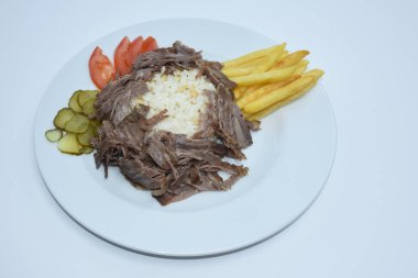 Top view of Iskender doner kebab with rice, fried potatoes, tomatoes and pickled cucumbers served on a white plate
