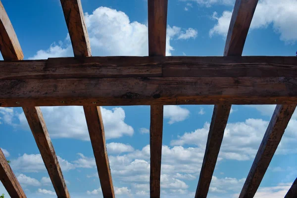 An incomplete wooden roof skeleton in nature with sky and clouds frame, tree branches in the sky. Roof repairing.