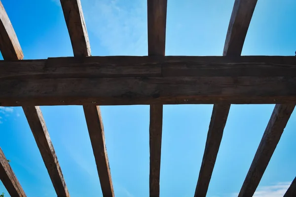 An incomplete wooden roof skeleton in nature with sky and clouds frame, tree branches in the sky. Roof repairing.