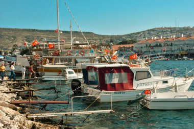 Foca, zmir, Turkey  29 Jun 2021. Wooden boats in the harbor in Foa, people looking at the sea, tour boats, Turkish flags and restaurants, mountains  across 