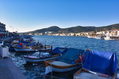 Foca, Izmir, Turkey 29 Jun 2021 Fishing boats with Turkish flags along the coastline of Foca holiday resort, cafe, hotels and restaurants on the opposite shore. Aegean town of Izmir.