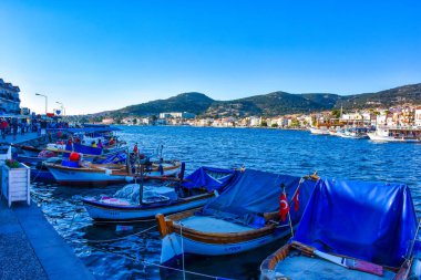 Foca, Izmir, Turkey 29 Jun 2021 Fishing boats with Turkish flags along the coastline of Foca holiday resort, cafe, hotels and restaurants on the opposite shore. Aegean town of Izmir.