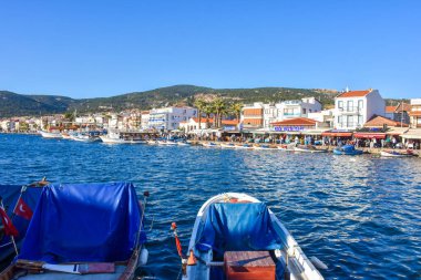 Foca, Izmir, Turkey 29 Jun 2021 Fishing boats with Turkish flags along the coastline of Foca holiday resort, cafe, hotels and restaurants on the opposite shore. Aegean town of Izmir.