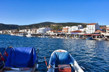Foca, Izmir, Turkey 29 Jun 2021 Fishing boats with Turkish flags along the coastline of Foca holiday resort, cafe, hotels and restaurants on the opposite shore. Aegean town of izmir.