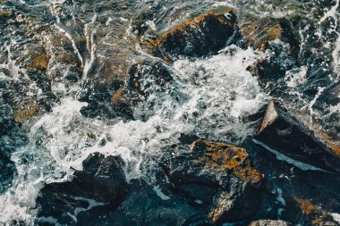 Sea waves crash against the rocks in the sea and create white foam. Top view of sea waves crashing the rocks in the Aegean sea