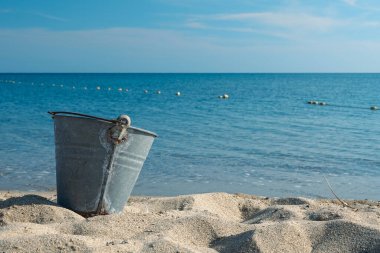 An empty beach metal bucket or bin on the beach among sands. 1960's summer concept. Water pollution clipart