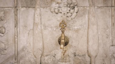Brass faucet on a fountain with patterned marble wall, a public bronze faucet fountain in the old Ottoman traditional style. Vintage public fountain wallpaper