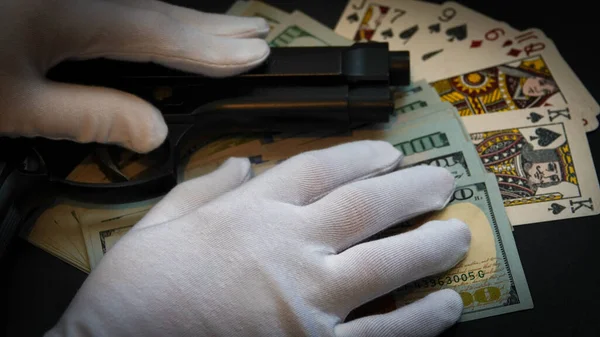 A woman with  white gloves touching gun, money and playing cards on a table