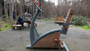 Yaşlı bir adam halka açık bir parkta ahşap spor malzemeleriyle egzersiz yaptıktan sonra dinleniyor.