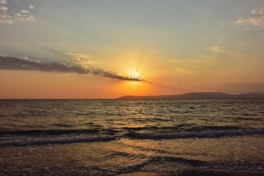 İzmir 'in Seferihisar ilçesi üzerinde güzel Ege gün batımı turuncu bir akşam gökyüzü ve sakin deniz dalgalarına yansıyan ışık