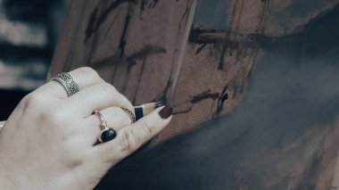 Şövalede fırça tutan genç bir ressamın eli. Çalışmanın başında, pastel renkler üzerine bir arkaplan hazırlar..