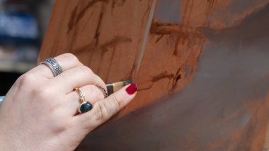 Şövalede fırça tutan genç bir ressamın eli. Çalışmanın başında, pastel renkler üzerine bir arkaplan hazırlar..