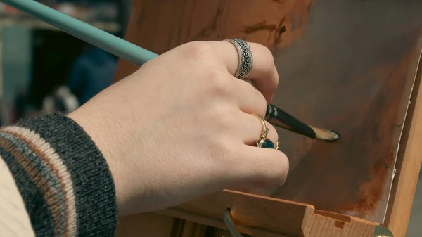 一个手握画笔在画架上的年轻画家的手 在工作开始时 她准备了一个彩色的背景 — 图库照片