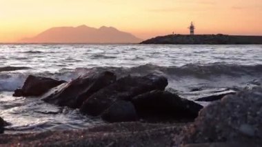 Kalekoy limanı Gkeada 'dan Semendirek Adası' na doğru deniz manzaralı günbatımı manzaralı. Deniz fenerinin yanında yavaşça yürüyen bir adam. Çanakkale Türkiye 'si.