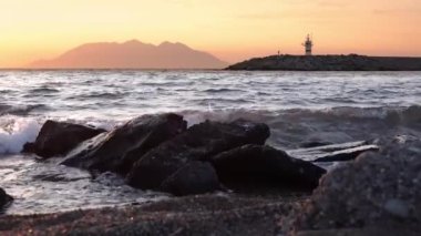 Kalekoy limanı Gkeada 'dan Semendirek Adası' na doğru deniz manzaralı günbatımı manzaralı. Deniz fenerinin yanında yavaşça yürüyen bir adam. Çanakkale hindisi. Yavaş çekim 4k